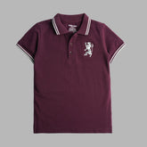 A burgundy short sleeve polo t-shirt for boys with a white collar and a white embroidered emblem on the chest.