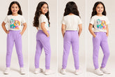 Young girl modeling a white t-shirt with a cartoon design and purple pants in front of a plain background.