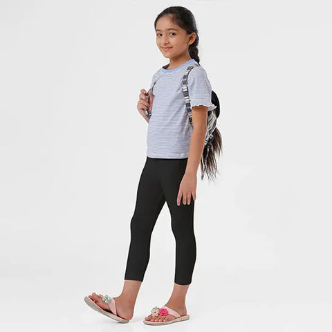 A young girl wearing a gray shirt and black leggings, standing against a white background.