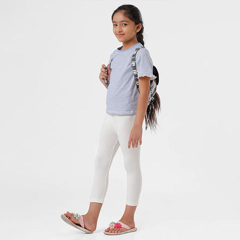 A young girl wearing white leggings and a grey t-shirt, standing against a white background.